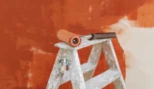 A close-up of a painting project in progress, featuring a paint roller resting on a ladder against a rich, earthy terracotta surface—one of the top trending creative accent walls for modern homes.