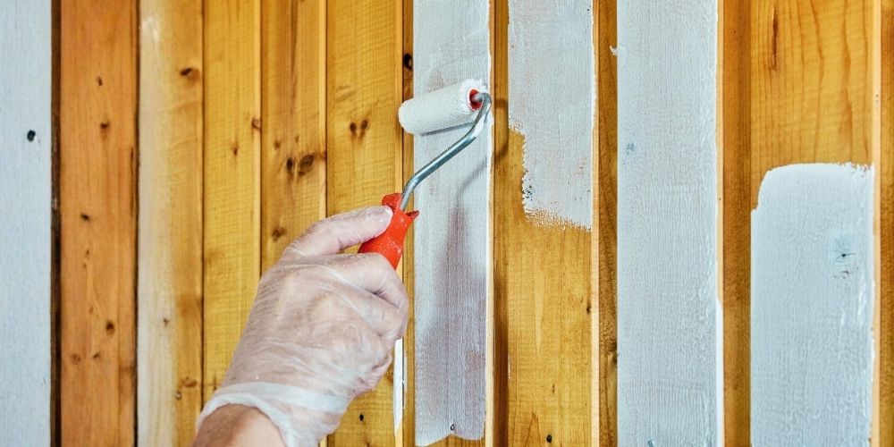 house painter using a roller to apply white paint to wooden panels