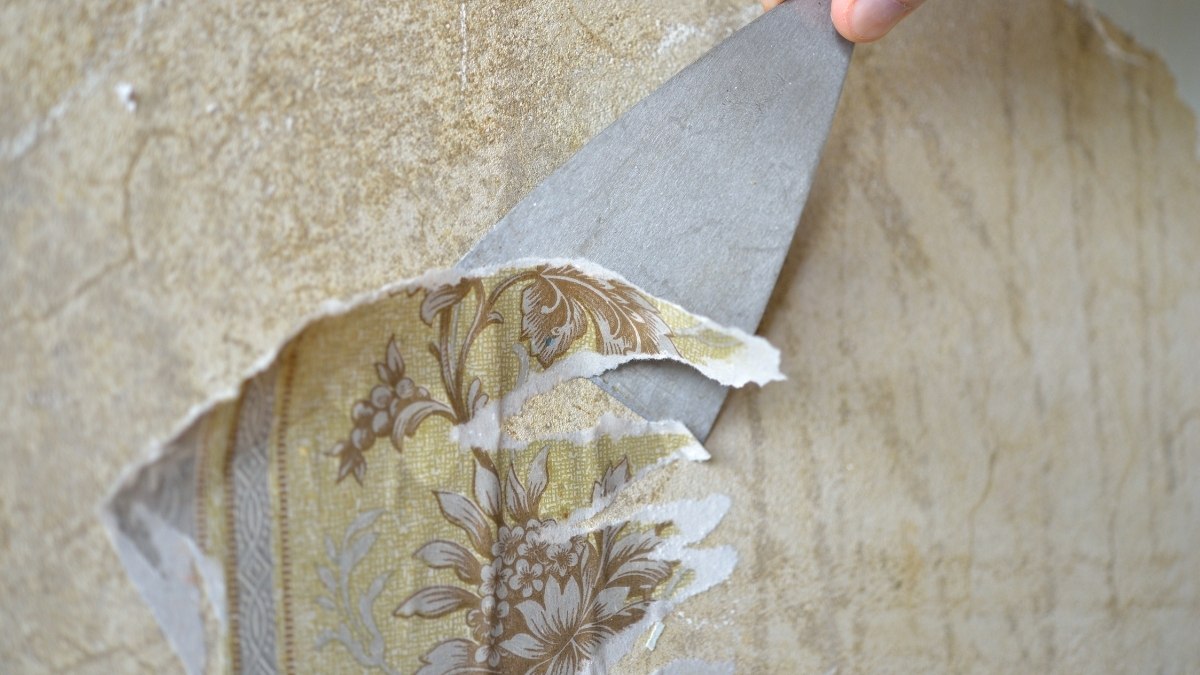 using a metal scraper to peel old, patterned wallpaper off